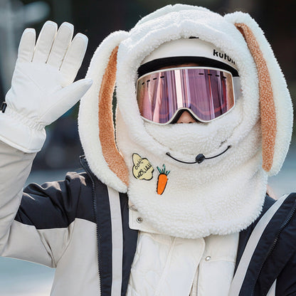 Person wearing a fluffy bunny hood with goggles and carrot design, waving outdoors.
