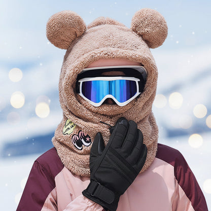 Person wearing a brown bear-themed hood with goggles and gloves in an winter setting